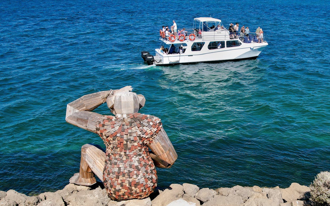 Tour boat on ocean near large wooden sculpture during Giant & Dolphin Sightseeing Cruise.