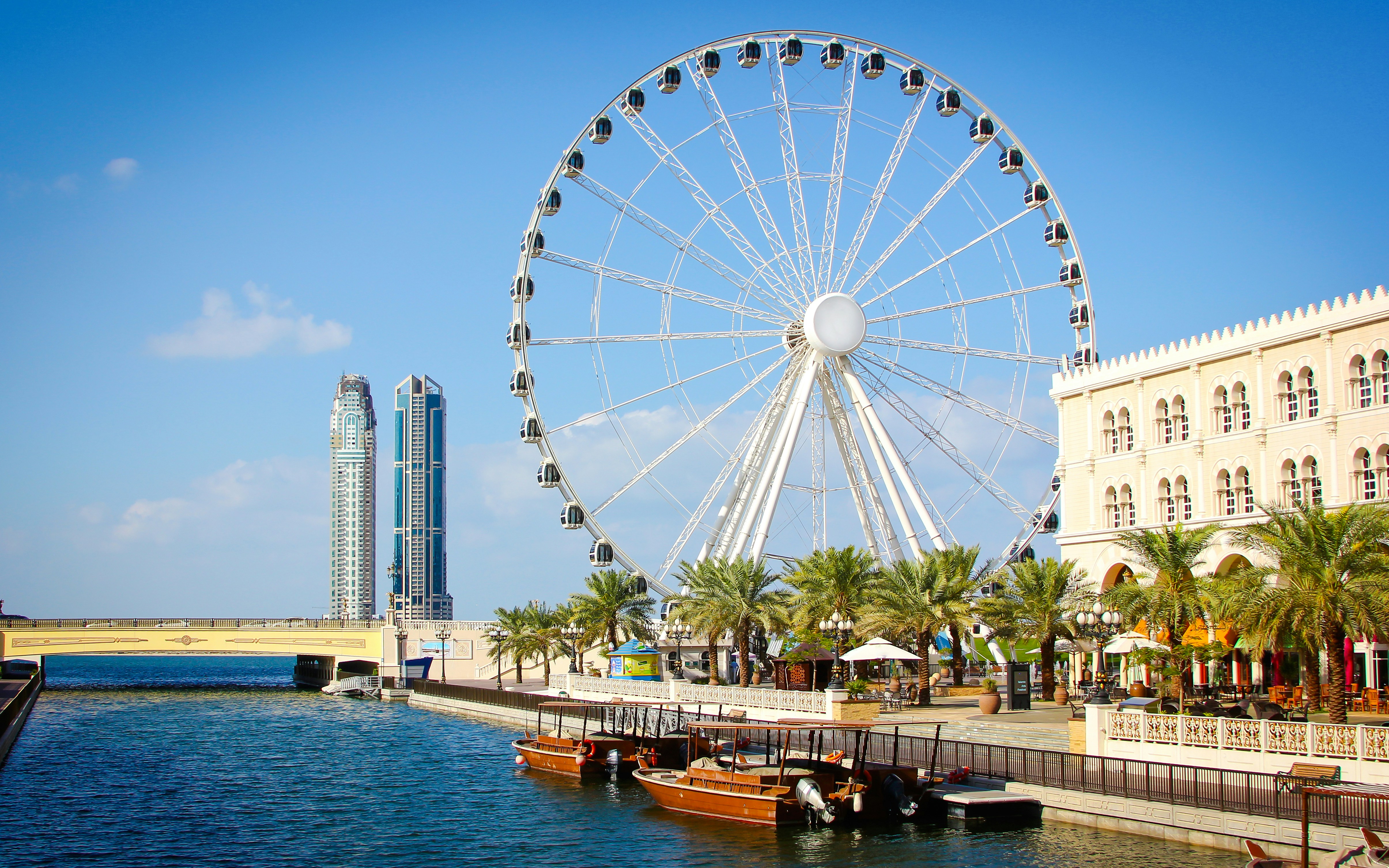 Ferris wheel by the canal in Al Qasba, Sharjah with nearby buildings and boats.