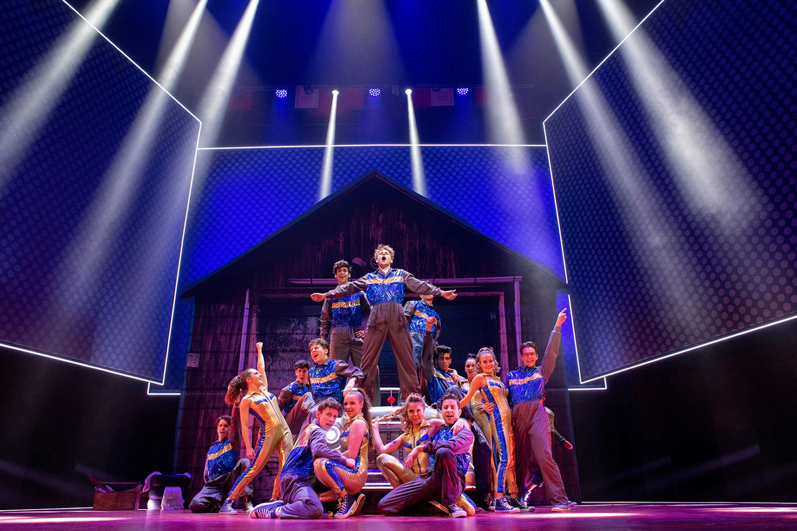 Performers on stage in a dynamic scene from the musical "Grease" with vibrant lighting.