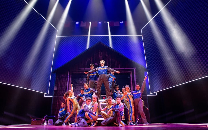 Performers on stage in a dynamic scene from the musical "Grease" with vibrant lighting.