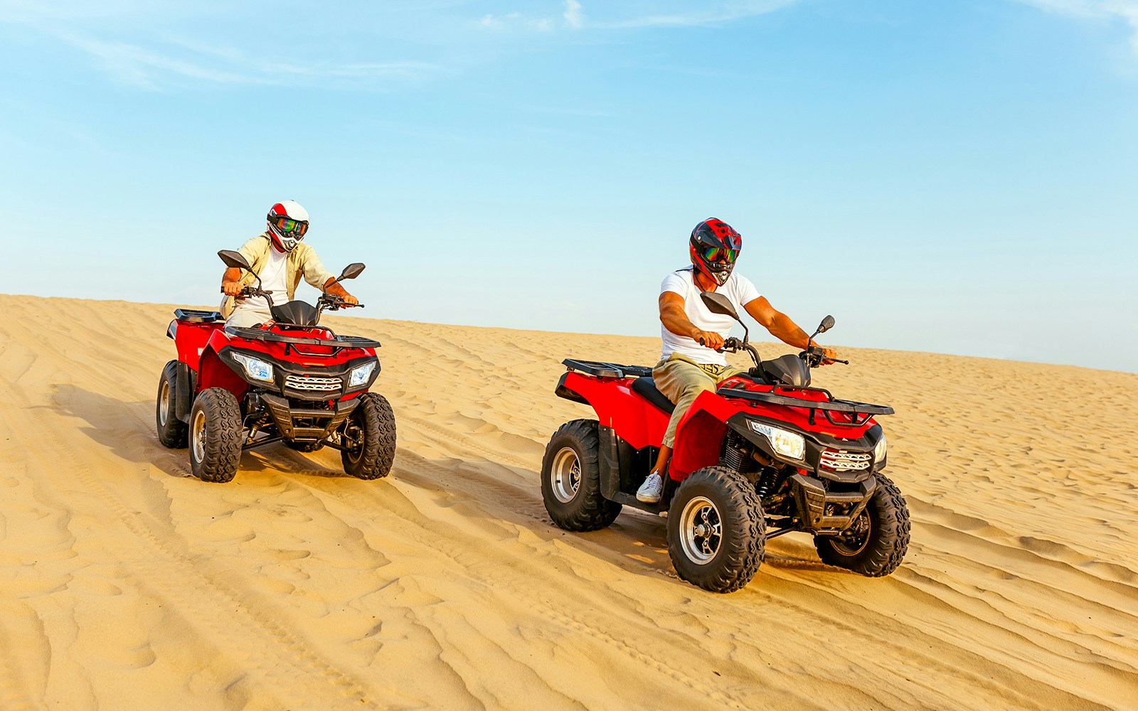 Two quad bikes driving on sand dunes in Dubai desert.