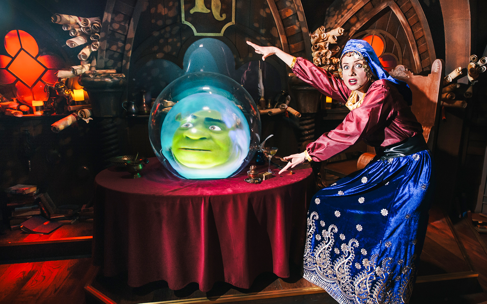 Shrek's face in a crystal ball at Shrek's Adventure, London, with a performer gesturing.
