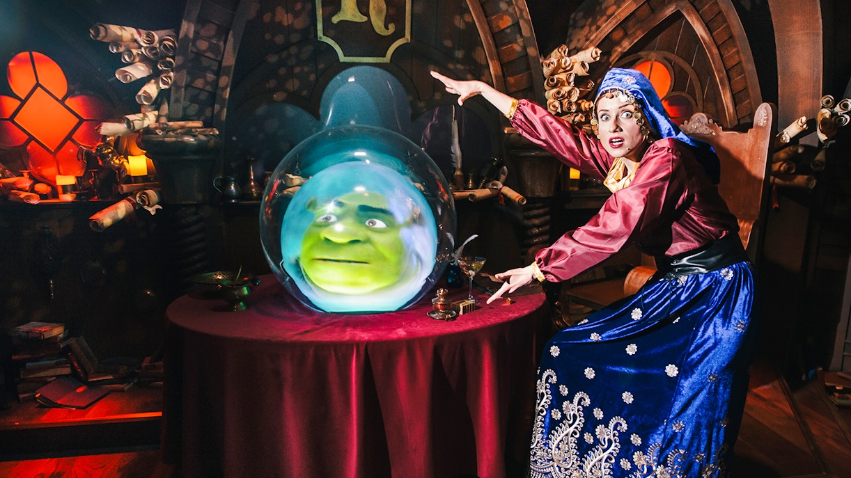 Shrek's face in a crystal ball at Shrek's Adventure, London, with a performer gesturing.