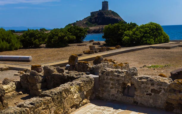 Nora Archaeological Site ruins with a coastal tower in the background, Sardinia.