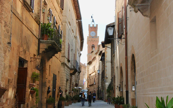 Narrow street in Tuscany with historic buildings and a clock tower in the distance.