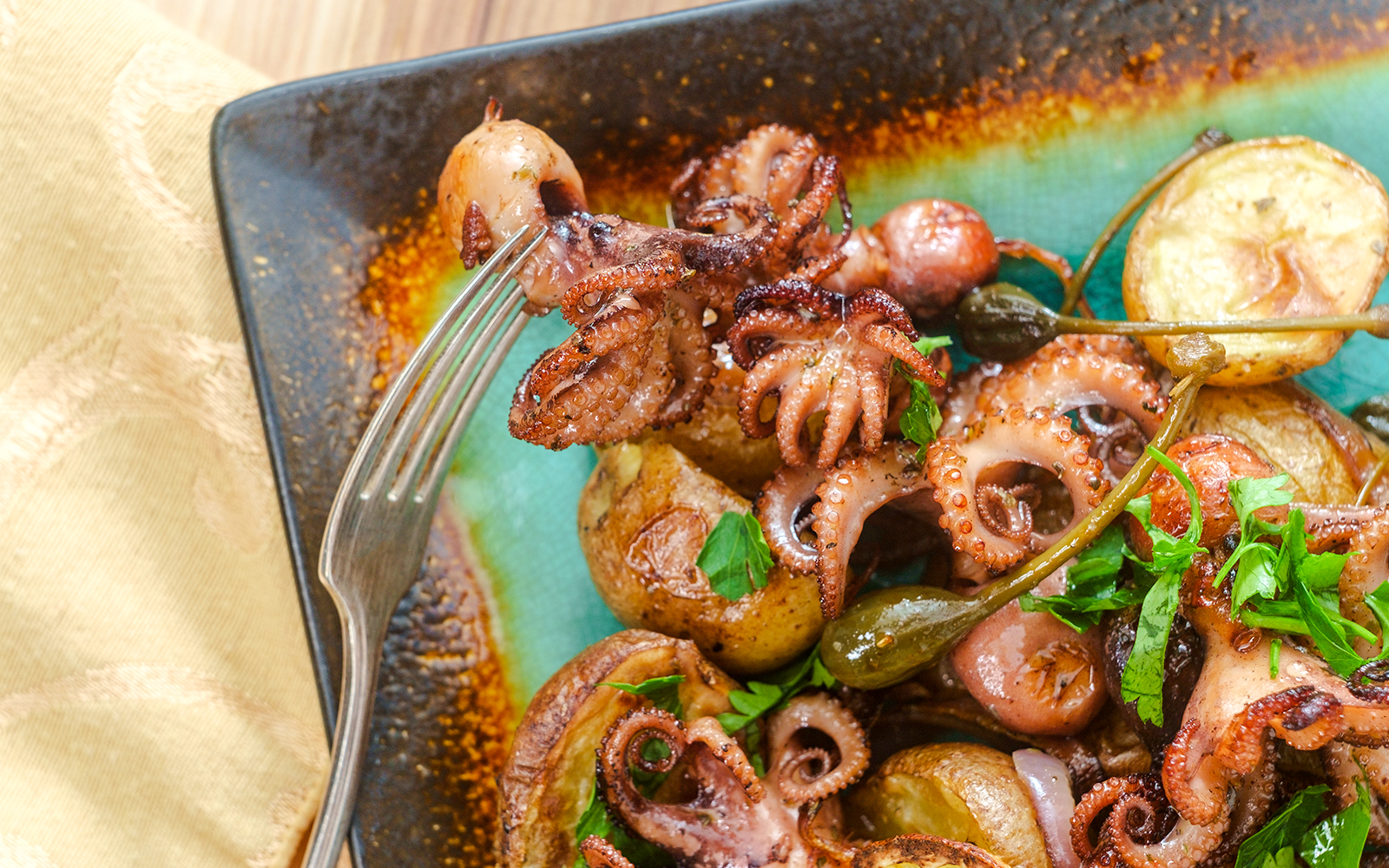 Portuguese octopus a lagareiro with potatoes and herbs on a plate.