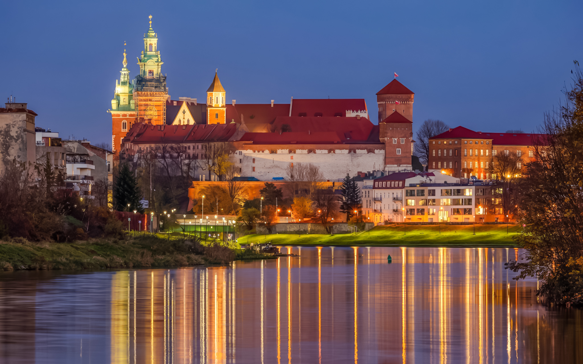 Wawel Royal Castle and Cathedral complex illuminated at night, reflected in the Vistula River, Kraków, Poland.
