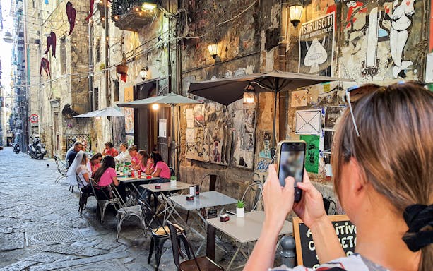 Outdoor cafe scene in Naples with people dining and street art on walls.