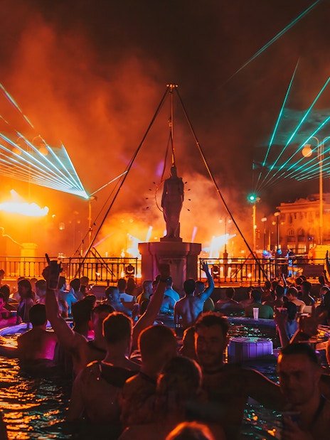 Crowd enjoying Sparty bath party with lights and music at Széchenyi Thermal Bath, Budapest.