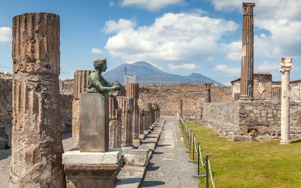 Tourists walking through ancient ruins of Pompeii with Mount Vesuvius in the background, Italy.
