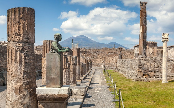 Tourists walking through ancient ruins of Pompeii with Mount Vesuvius in the background, Italy.