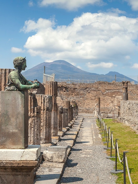 Tourists walking through ancient ruins of Pompeii with Mount Vesuvius in the background, Italy.