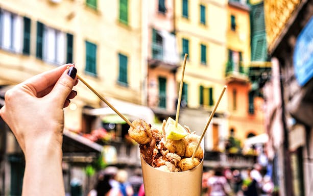 Skewered street food in Rome with colorful buildings in the background.