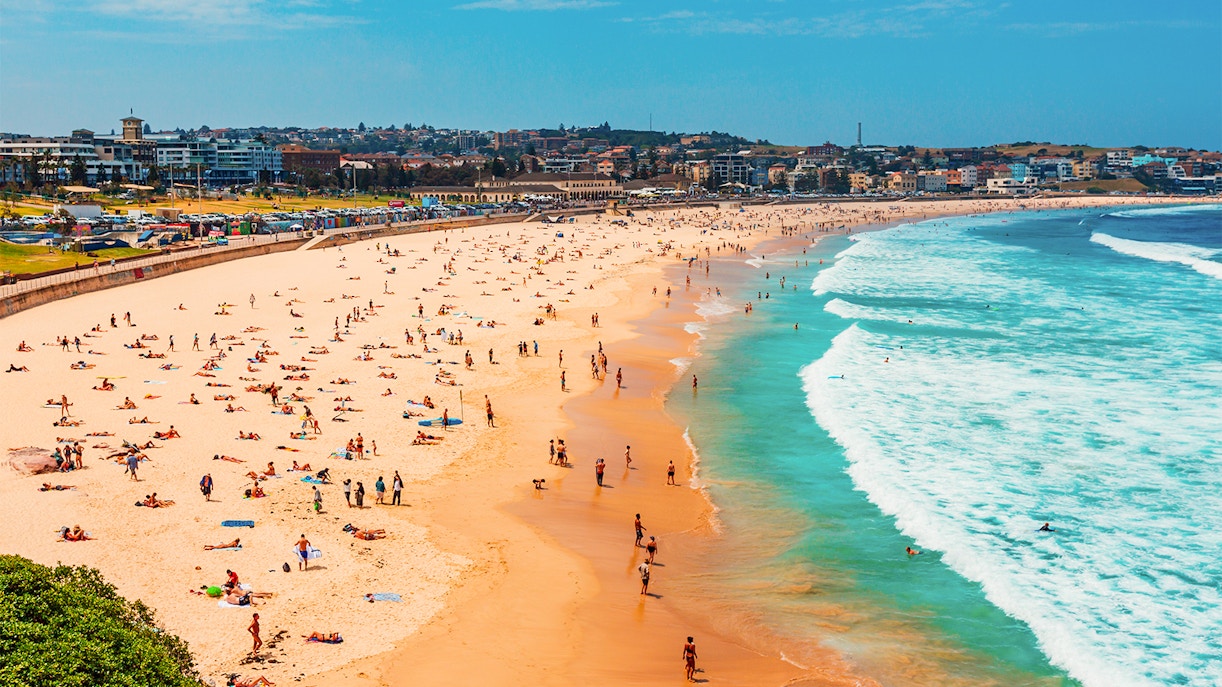 Crowded Bondi Beach in Sydney with people sunbathing and swimming.