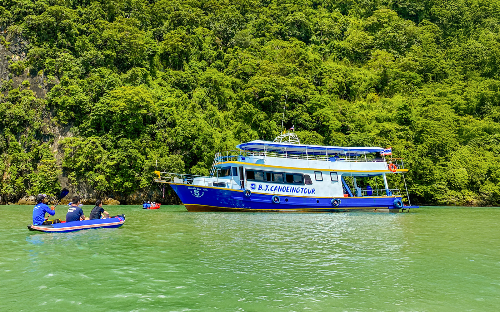 Tourists canoeing near a tour boat at Phang Nga Bay, surrounded by lush greenery.