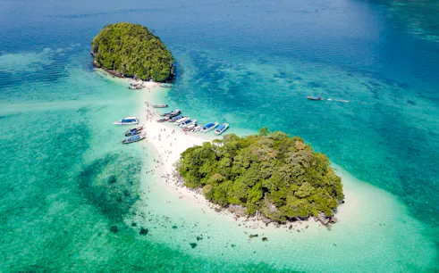 Longtail boats docked at a sandy beach between two islands in Krabi, Thailand.