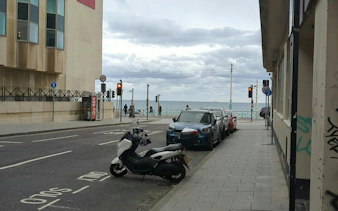 Street view near Brighton seafront with parked vehicles and pedestrians by the ocean.