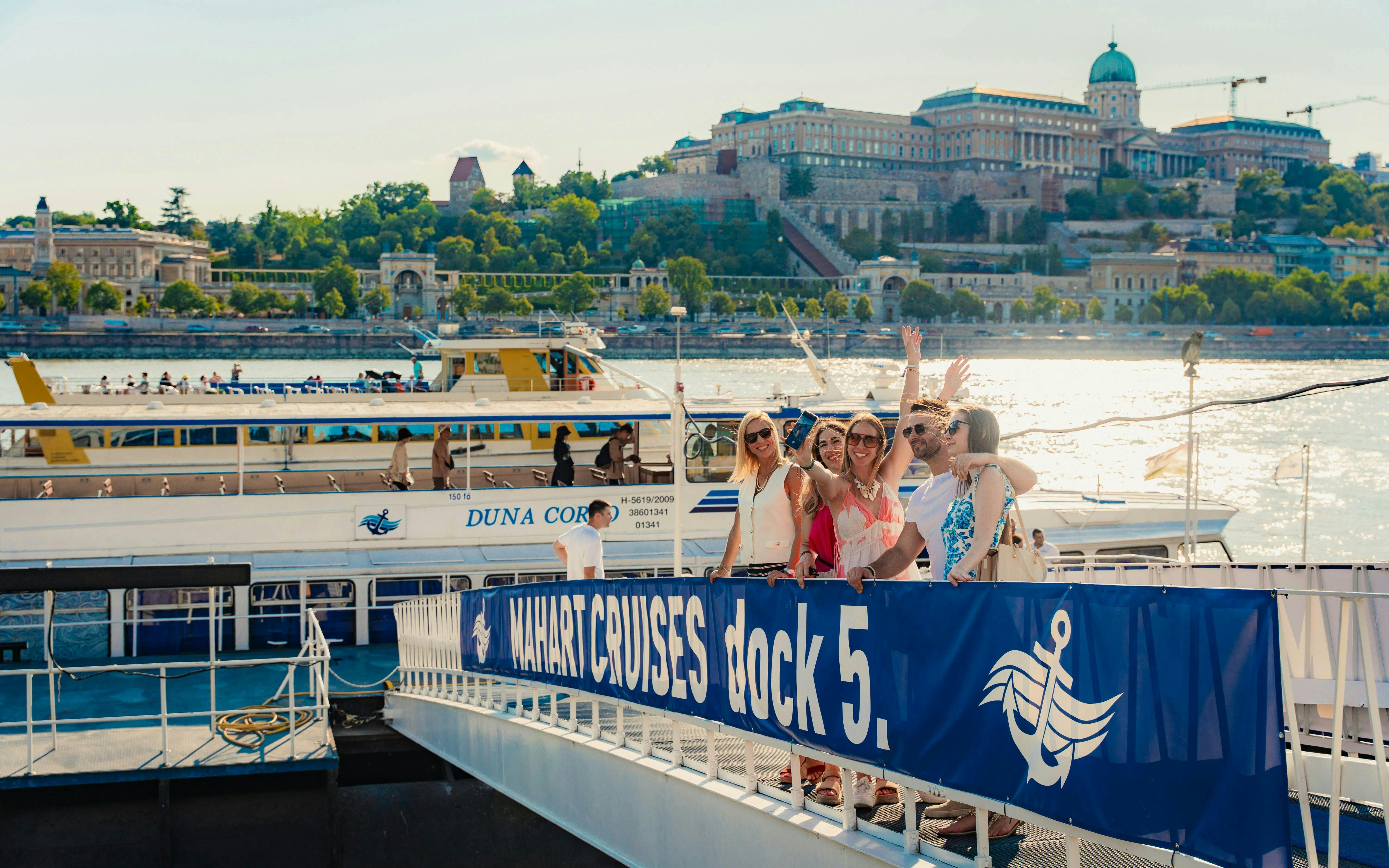 Tourists boarding a Budapest daytime hop-on hop-off cruise at dock 5 with Buda Castle in the background.