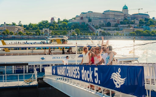 Tourists boarding a Budapest daytime hop-on hop-off cruise at dock 5 with Buda Castle in the background.