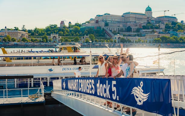 Tourists boarding a Budapest daytime hop-on hop-off cruise at dock 5 with Buda Castle in the background.