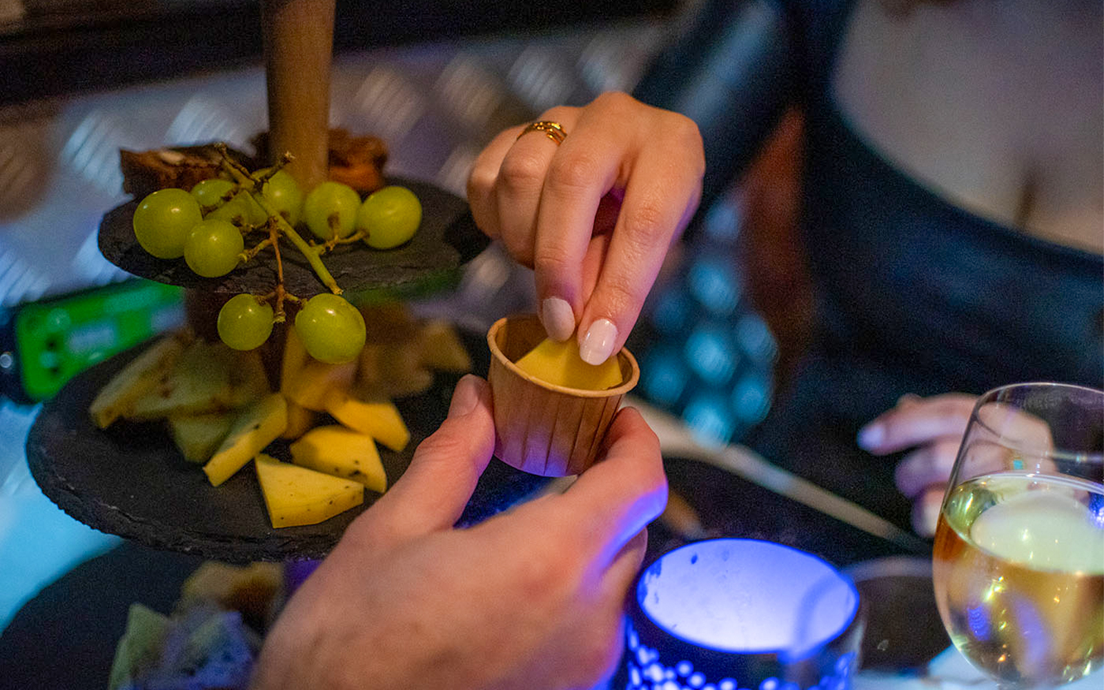 Hands reaching for cheese and grapes on a platter during Amsterdam canal cruise with wine.
