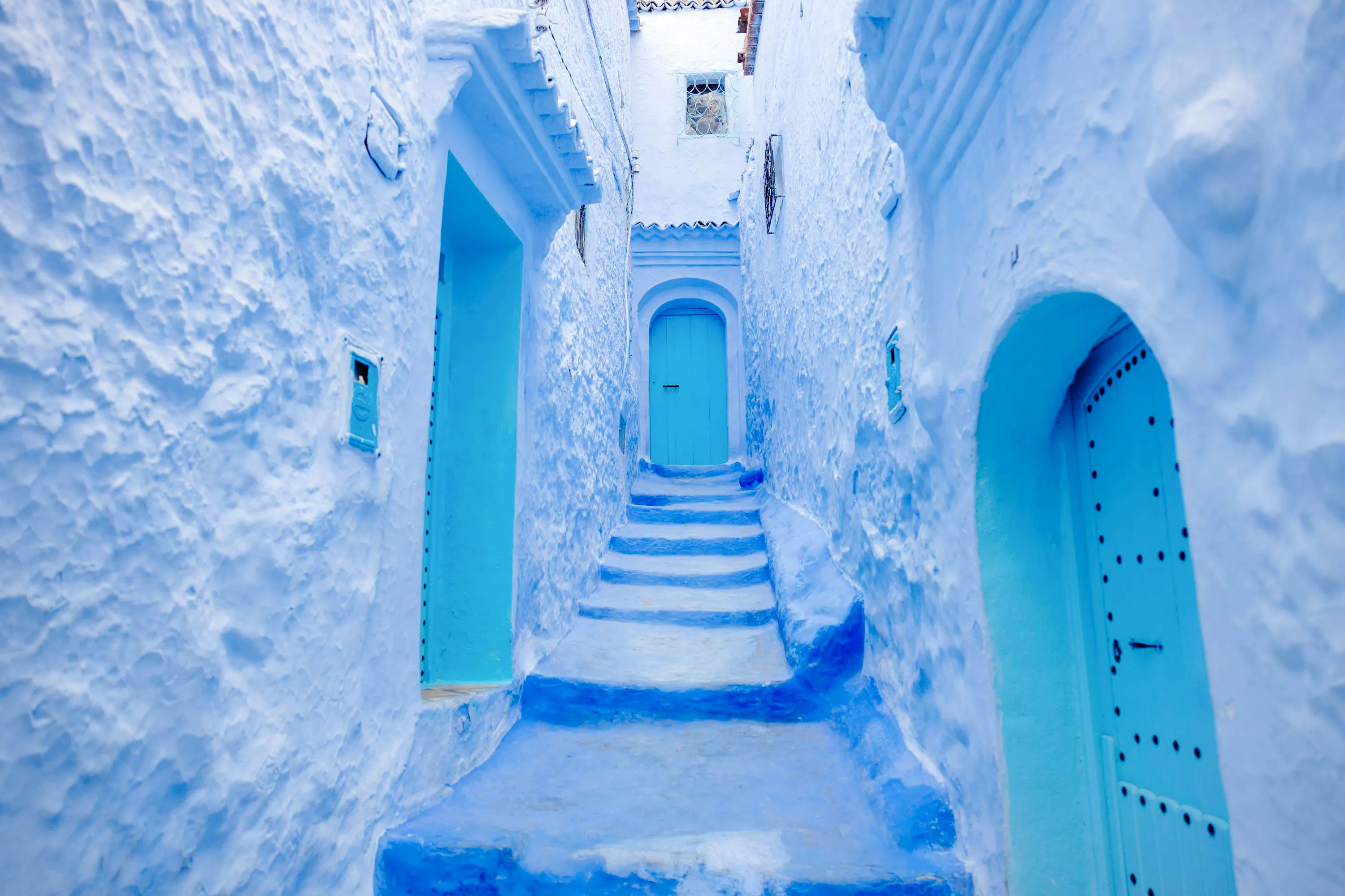 Narrow blue alleyway in Chefchaouen, Morocco, with blue-painted buildings and steps.