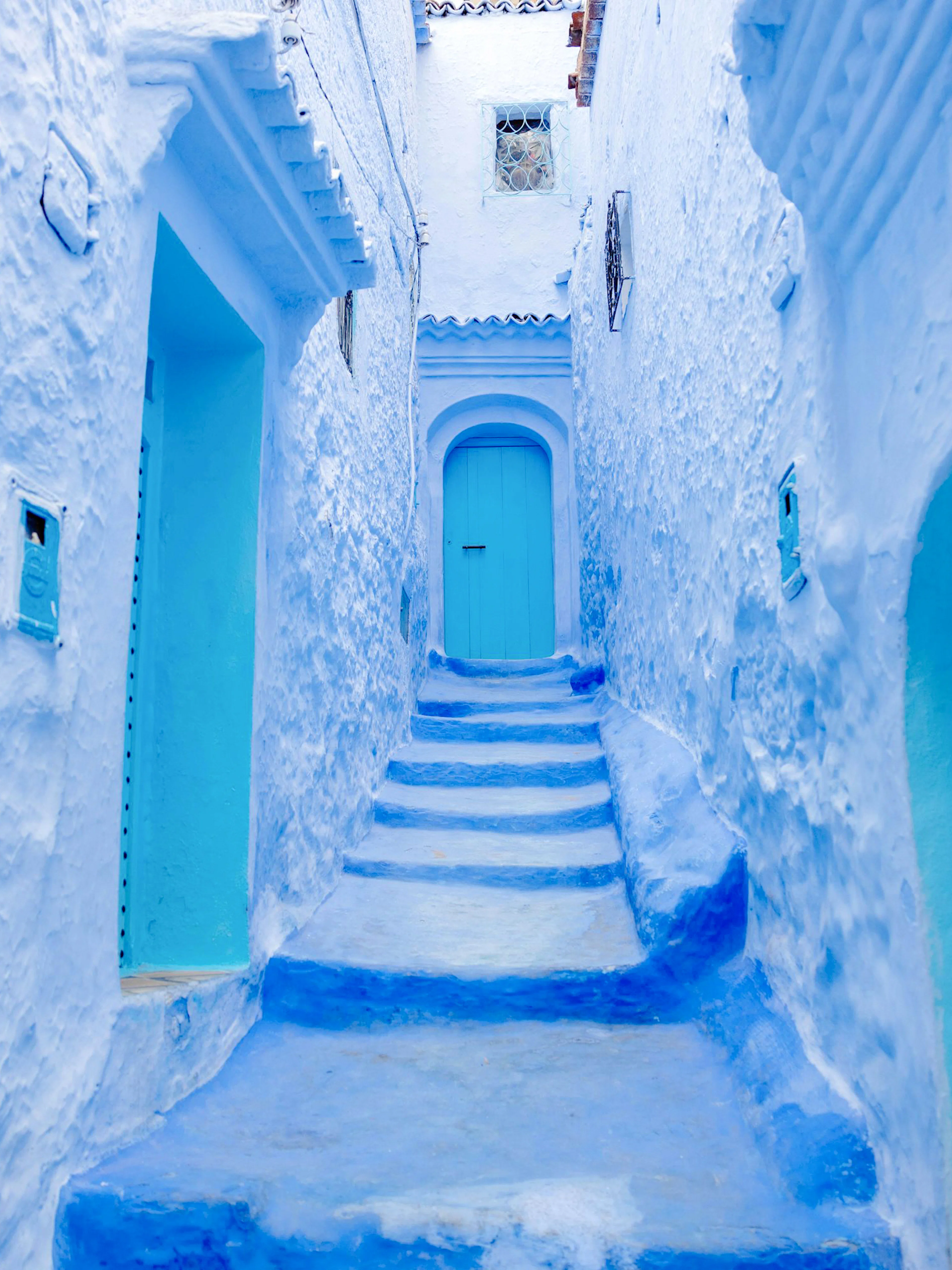 Narrow blue alleyway in Chefchaouen, Morocco, with blue-painted buildings and steps.