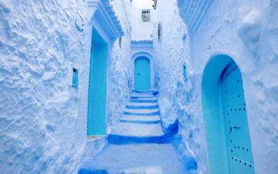 Narrow blue alleyway in Chefchaouen, Morocco, with blue-painted buildings and steps.