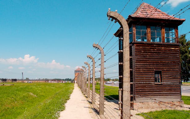Auschwitz-Birkenau concentration camp fence and watchtower under blue sky.