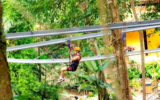 Person ziplining through lush forest at SKY ROCK eco-adventure in Thailand.