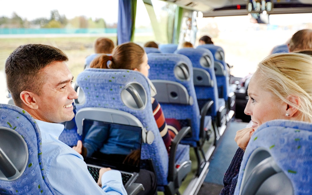 Group of passengers smiling and chatting on a travel bus.