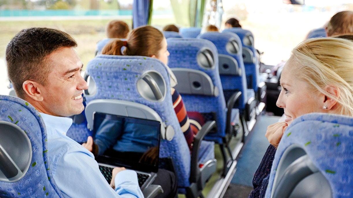 Group of passengers smiling and chatting on a travel bus.