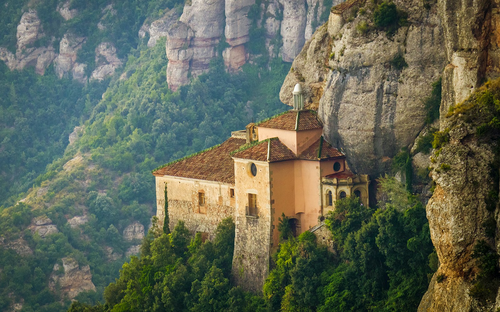 Historic building nestled in the cliffs of Cueva de la Moreneta, surrounded by lush greenery.
