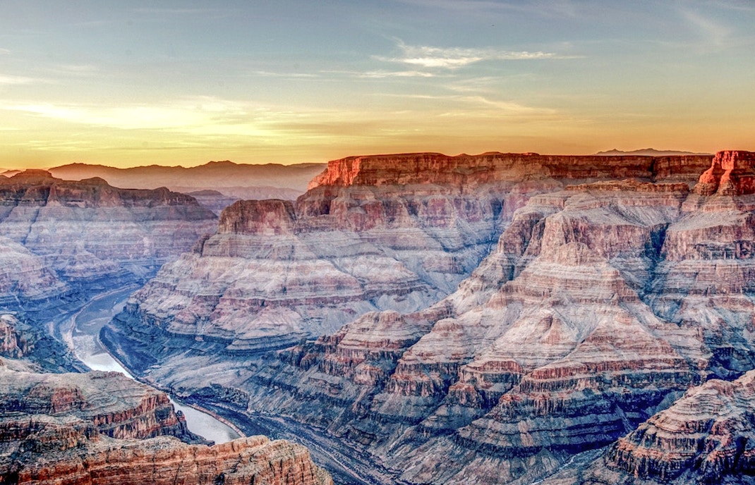 Grand Canyon West Rim at sunset with layered rock formations and river below.