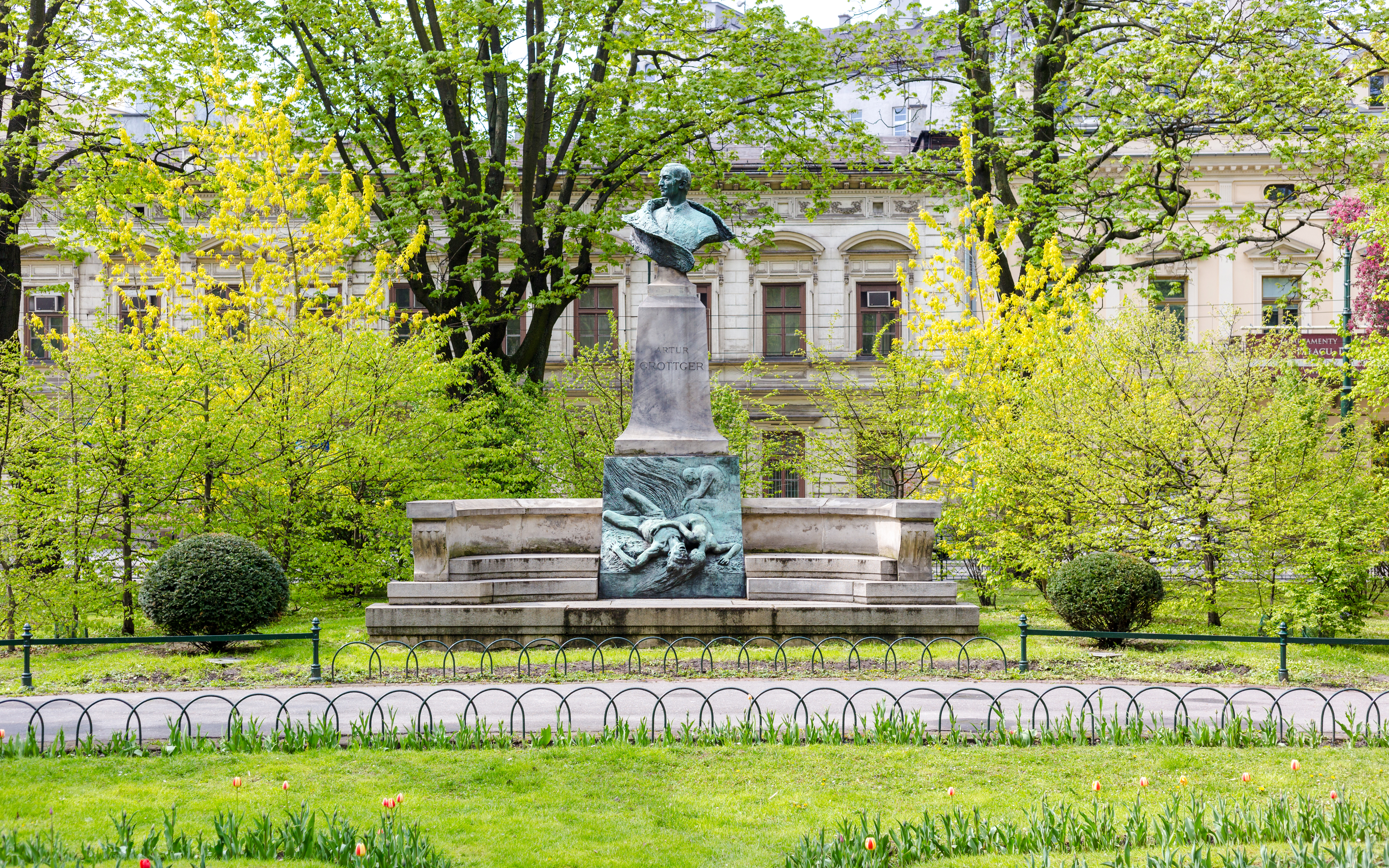 Statue of Artur Grottger in Planty Park, Krakow, surrounded by lush greenery.