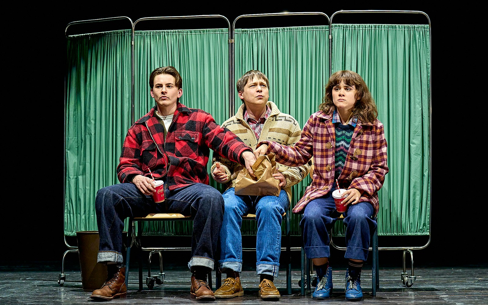Three people sitting on stage in front of green curtains, part of "Stranger Things: The First Shadow.