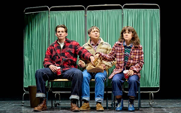 Three people sitting on stage in front of green curtains, part of "Stranger Things: The First Shadow.
