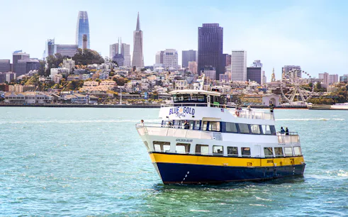 Blue and Gold Fleet ferry cruising in San Francisco Bay with city skyline in the background.