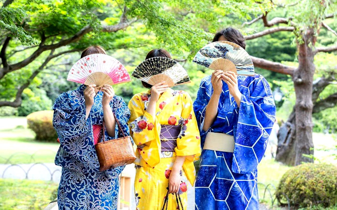 Kimono-clad individuals with fans in Shinjuku Gyoen National Garden, Tokyo.