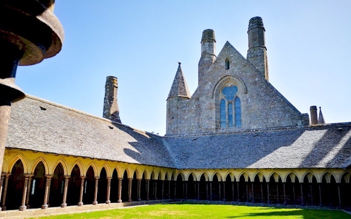Mont-Saint-Michel Abbey cloister with stone arches and green courtyard.