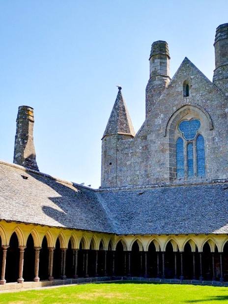 Mont-Saint-Michel Abbey cloister with stone arches and green courtyard.