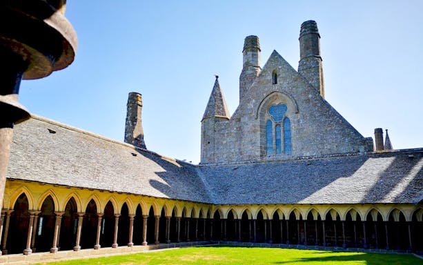 Mont-Saint-Michel Abbey cloister with stone arches and green courtyard.