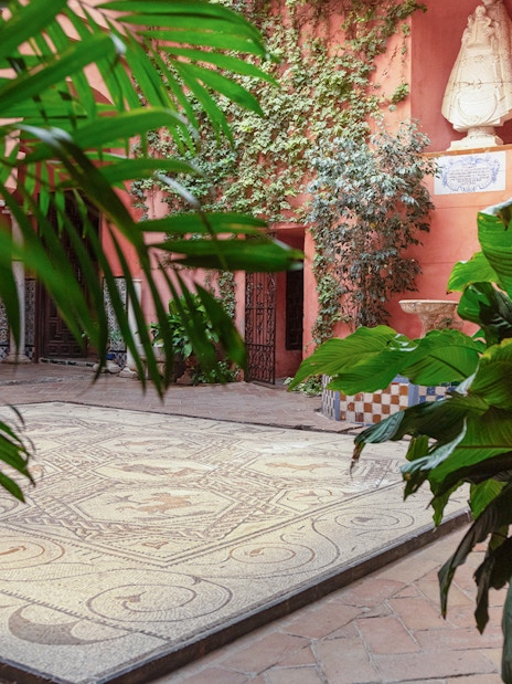 Courtyard with mosaic floor and lush plants at Casa de Salinas, Seville.