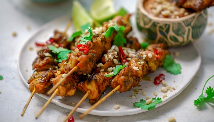 Chicken satay skewers garnished with peanuts and cilantro, served with dipping sauce.