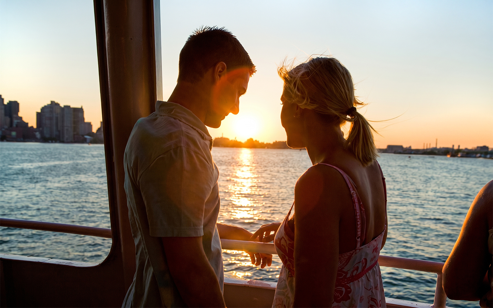 Couple enjoying sunset on a Boston sightseeing cruise with city skyline in view.