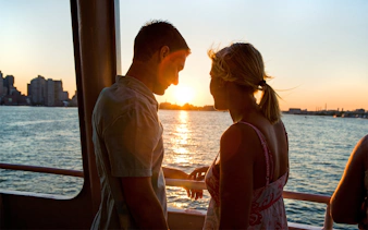 Couple enjoying sunset on a Boston sightseeing cruise with city skyline in view.