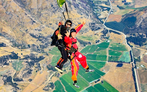 Tandem skydive over Wanaka landscape with fields and hills below.