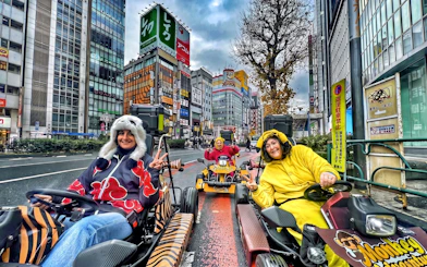 Go-kart riders in costumes driving through Shibuya, Tokyo with cityscape backdrop.