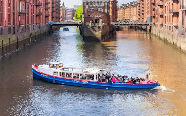 Harbor cruise boat with tourists on a canal in Hamburg's Speicherstadt district.
