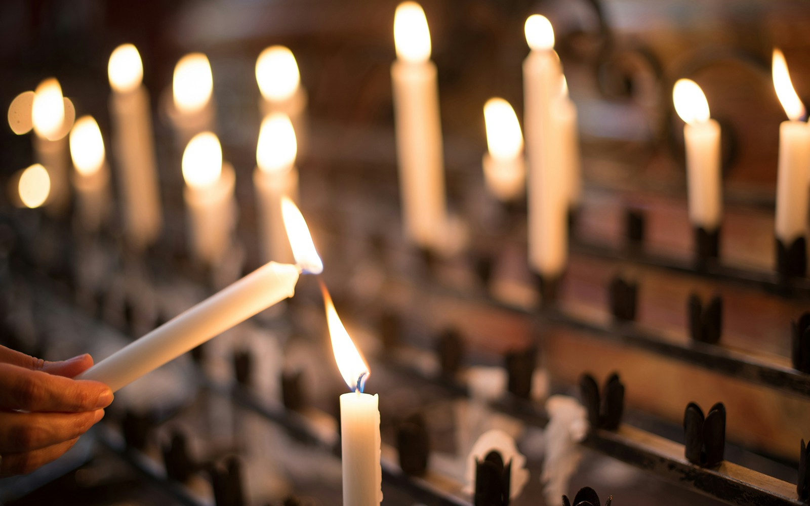 Woman lighting a candle in a dimly lit setting with multiple candles in the background.